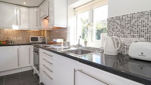 Una cocina moderna con armarios blancos, encimera negra, un fregadero, un microondas y un hervidor.