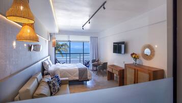 Quarto de hotel moderno com cama, área de estar, escrivaninha e uma grande janela com vista para o oceano.