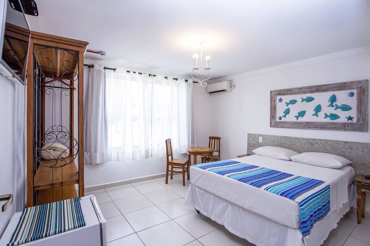 Un dormitorio con cama, un armario de madera, una mesa con sillas, una araña y una obra de arte colgada en la pared.