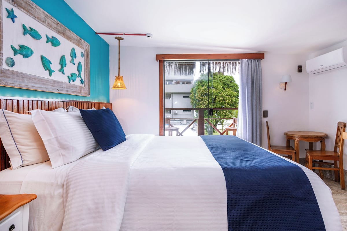 Habitación de hotel con una cama grande, vistas al balcón y un cuadro de peces en la pared.