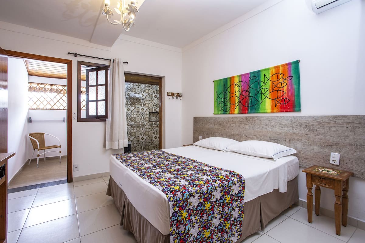 Un dormitorio con una cama, una mesita de noche de madera, una obra de arte colorida en la pared y vistas al balcón exterior.
