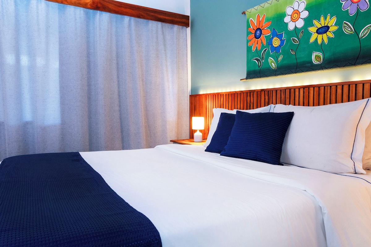Una habitación de hotel con cama, mesita de noche, lámpara y un mural floral en la pared.