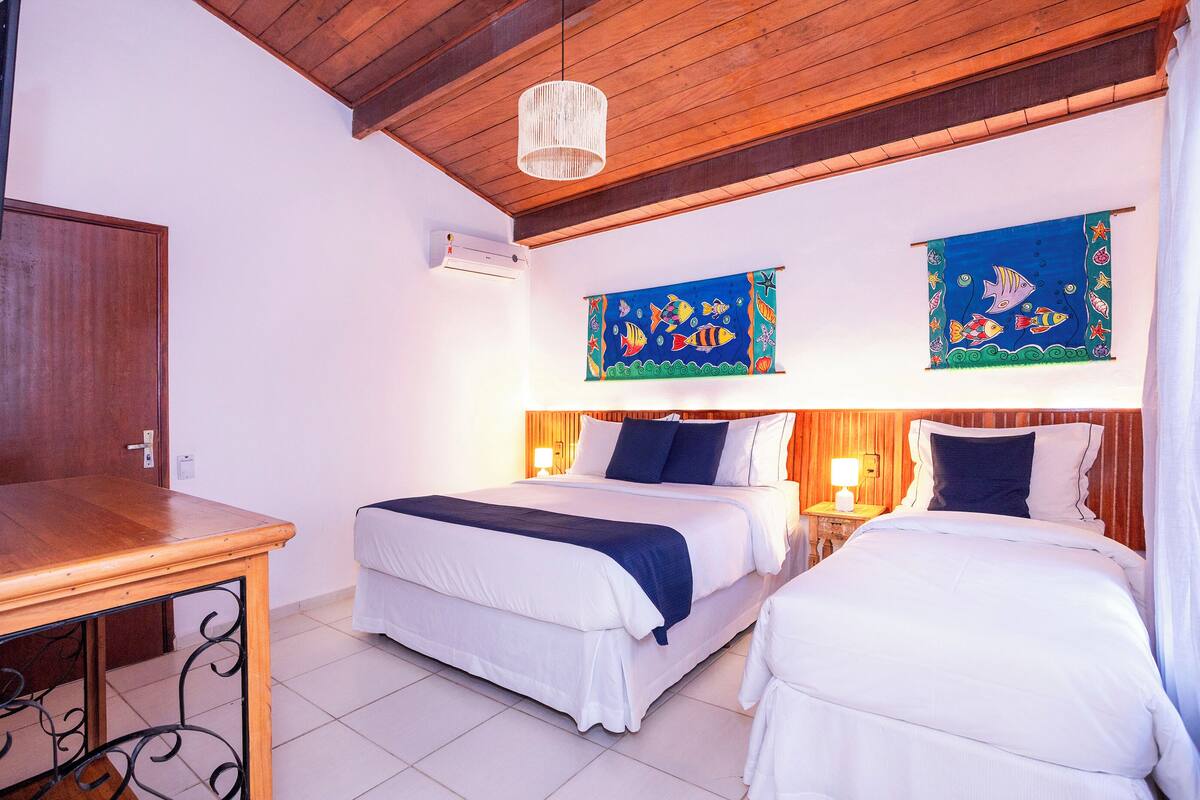 Habitación de hotel con dos camas, vigas de madera en el techo, lámpara colgante y coloridas obras de arte en las paredes.