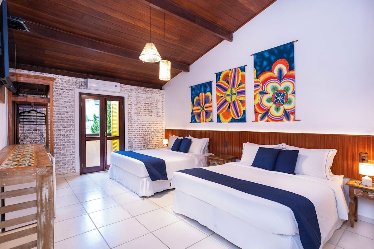 Habitación de hotel con dos camas, techo de madera y coloridos adornos en la pared.