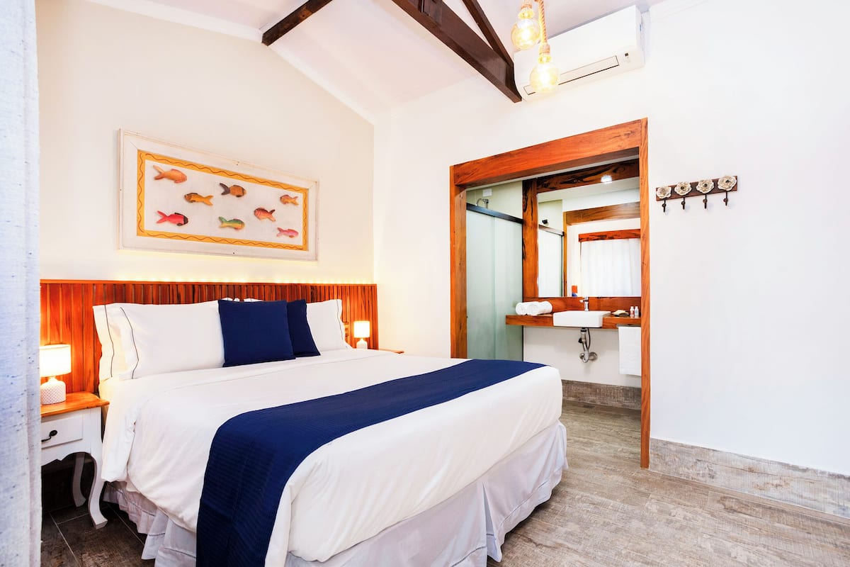 Habitación de hotel con una cama grande, cabecera de madera, adorno de pez montado en la pared, espejo y suelo de madera.