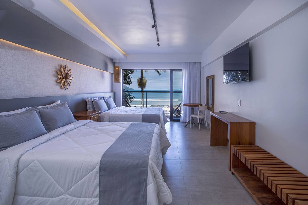 Una habitación de hotel moderna con dos camas, un escritorio y un ventanal con vistas al mar.