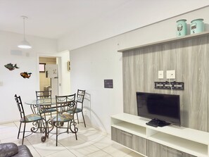 A modern living room with a dining area, a TV on a wooden TV stand, and decorative fish wall art.