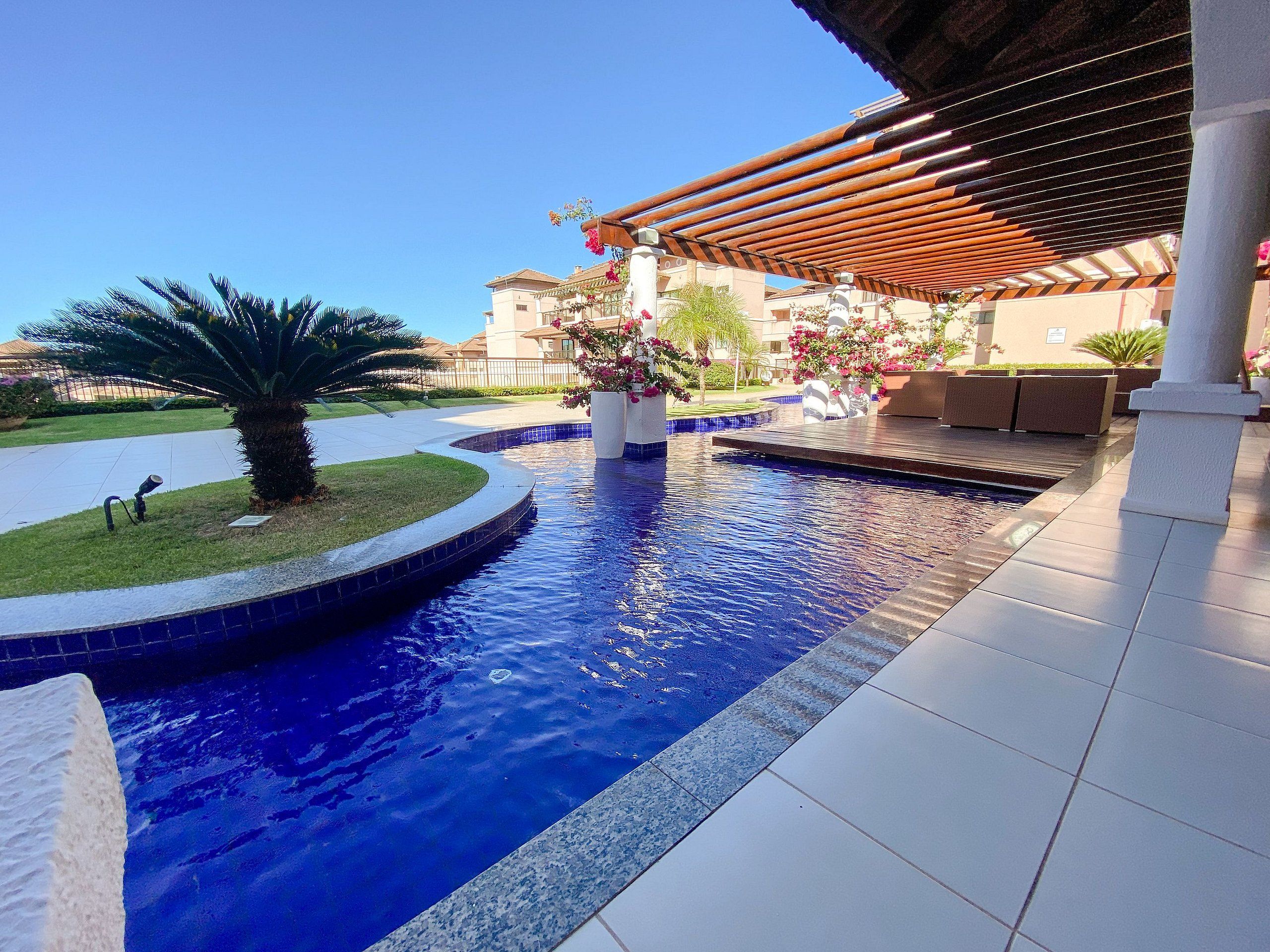 A swimming pool with a wooden pergola, a palm tree, and a flower planter.