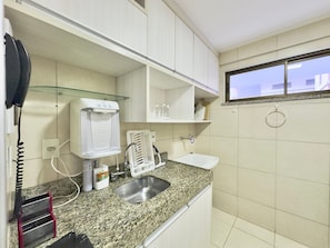 A kitchen with a granite countertop, a stainless steel sink, a coffee maker, and a window with a view of buildings.