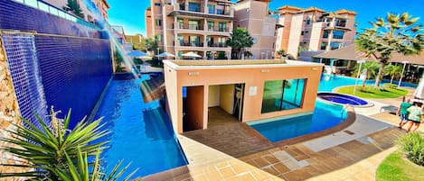 A hotel with a swimming pool, a covered area, and a view of other buildings.