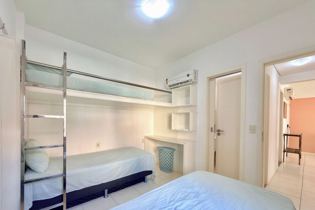 Une chambre avec des lits superposés, une petite table de chevet, une poubelle et un appareil de climatisation.