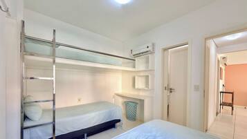 A room with bunk beds, a small bedside table, a trash bin, and an air conditioning unit.