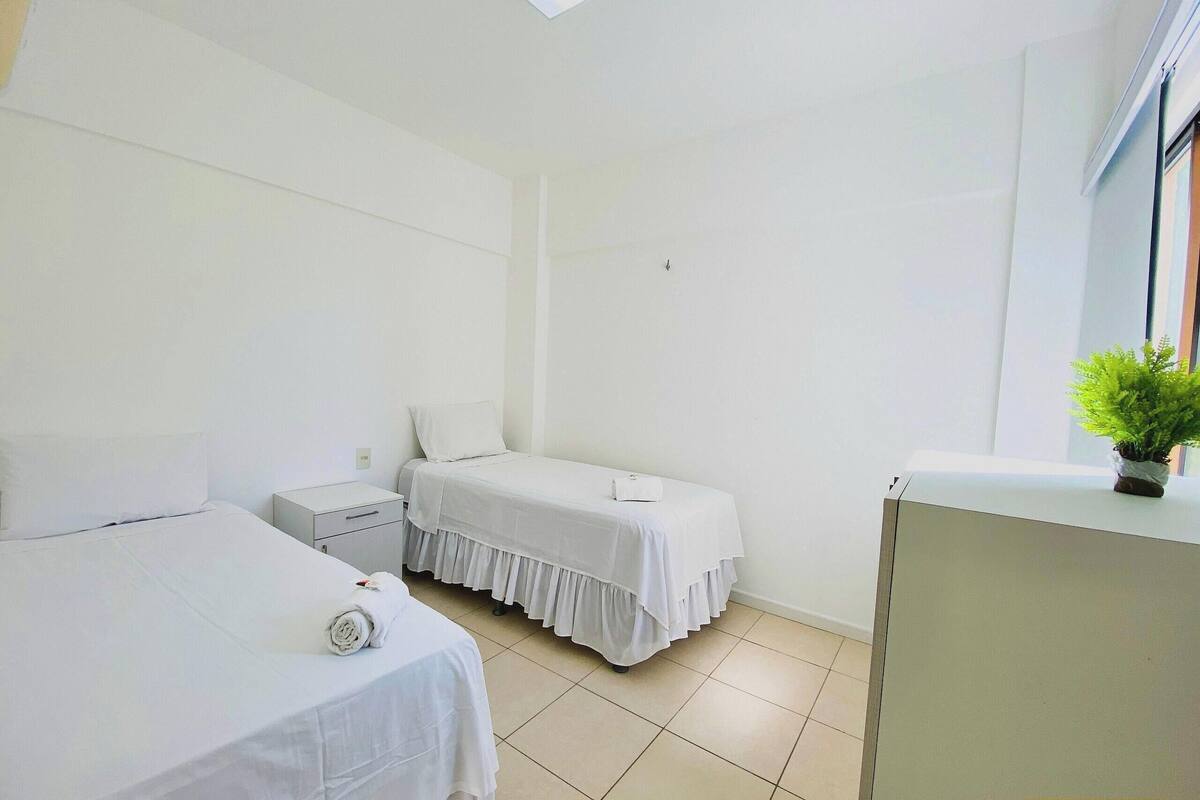 Habitación de hotel con dos camas, una mesita de noche, un armario pequeño y una planta en maceta.