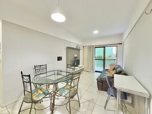 Een eetgedeelte met een glazen tafel en stoelen, een bank, een televisie en een balkon met uitzicht.