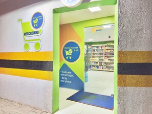 Entrada de una tienda con un letrero de carrito de compras, un letrero de servicio las 24 horas y un anuncio que indica que todos los productos están en un solo lugar.
