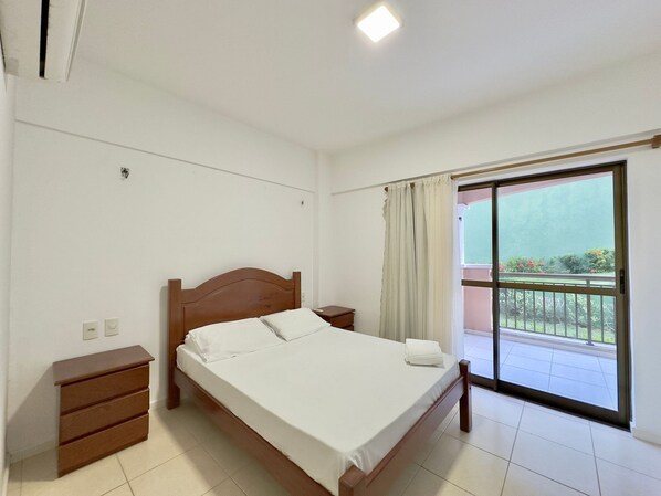 A bedroom with a wooden bed, a nightstand, a dresser, and a balcony with a view.
