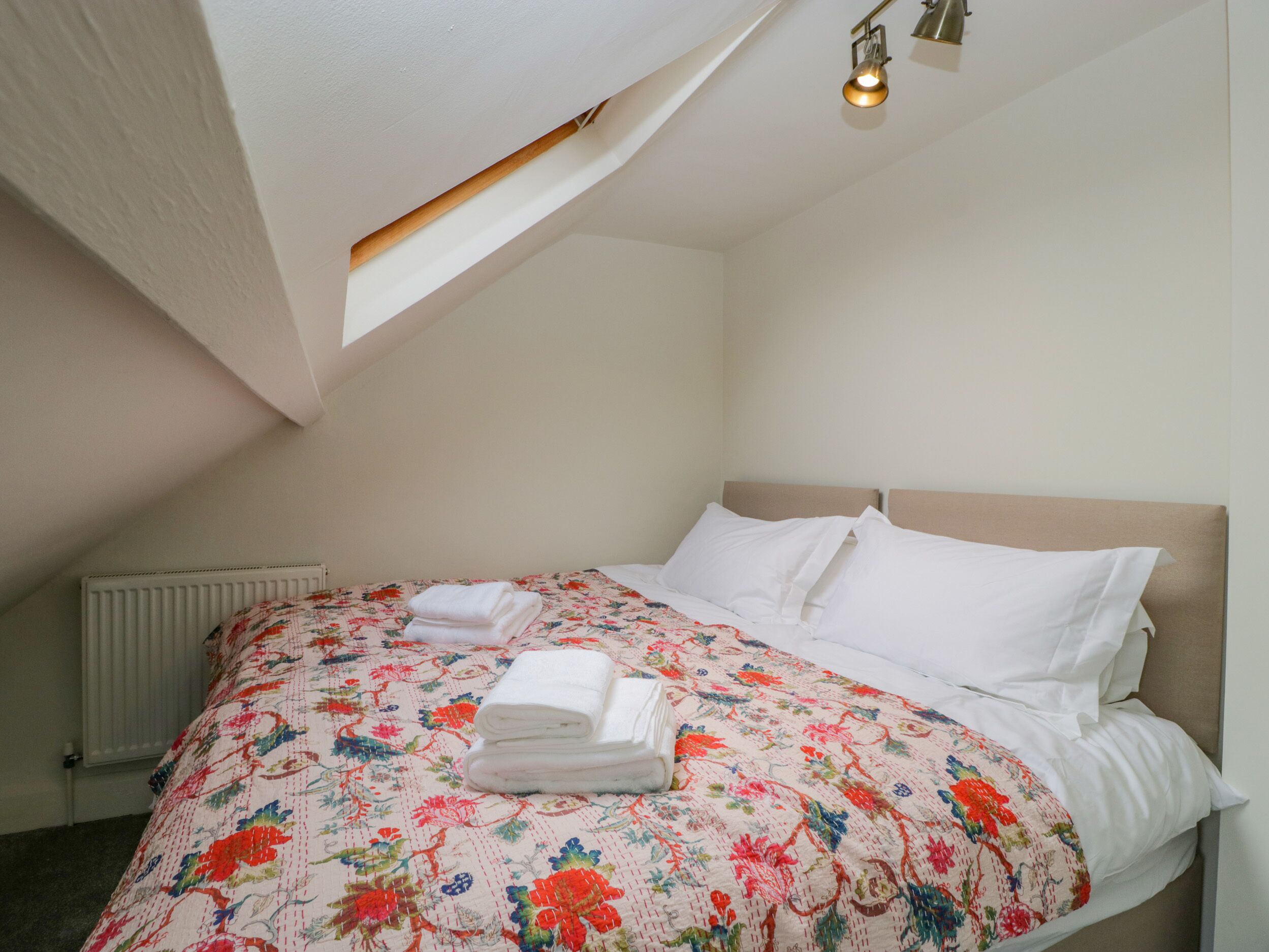 A bedroom with a sloped ceiling, a bed with floral bedding, white pillows, and a neatly folded towel on the bed.