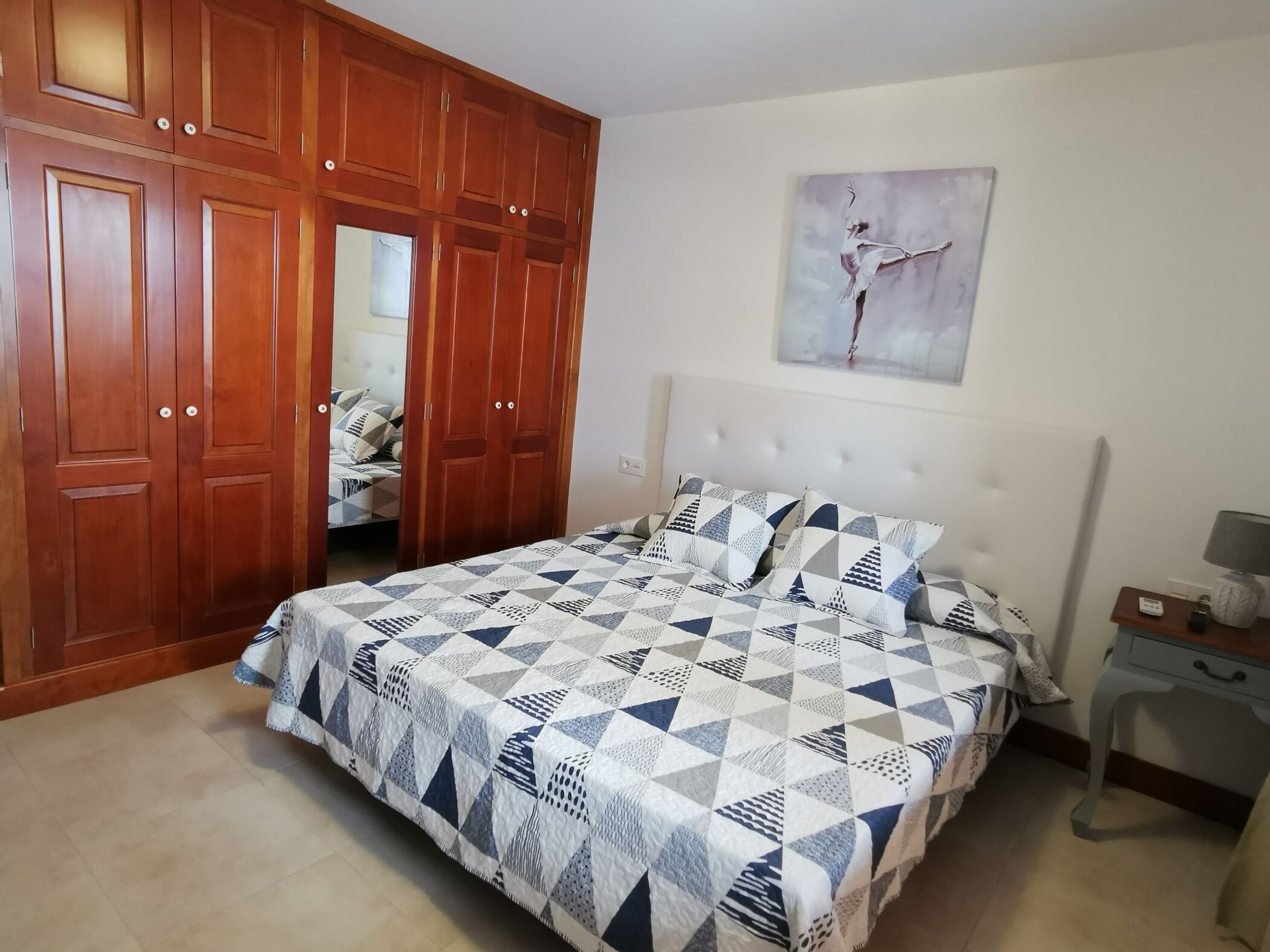 A bedroom with a bed, a wardrobe, a nightstand, and a painting on the wall.