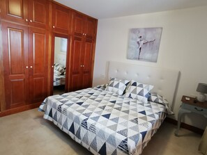 A bedroom with a bed, a wardrobe, a nightstand, and a painting on the wall.