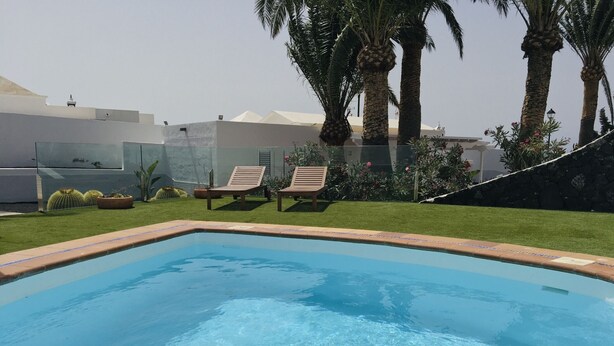 A rectangular swimming pool with clear blue water, surrounded by a well-maintained lawn and several palm trees. - One bedroom apartment with shared terrace (TAHICHE)