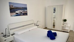 Habitación de hotel ordenada con cama, mesita de noche, armario y un cuadro colgado en la pared que representa una escena costera.