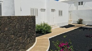 Un edificio blanco con un muro de piedra, un estrecho sendero y un pequeño jardín con flores rosadas.