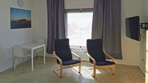 A room with two chairs, a small table, a TV mounted on the wall, and a window with curtains. - One bedroom apartment with balcony (TAHICHE)