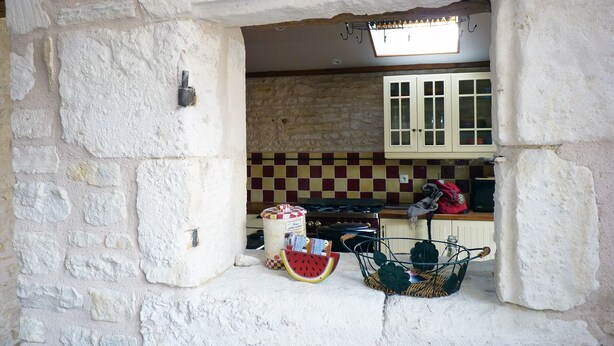 A rustic kitchen with stone walls, a checkered backsplash, and a window above the sink. - Le Petit Cloucq (Damvix)