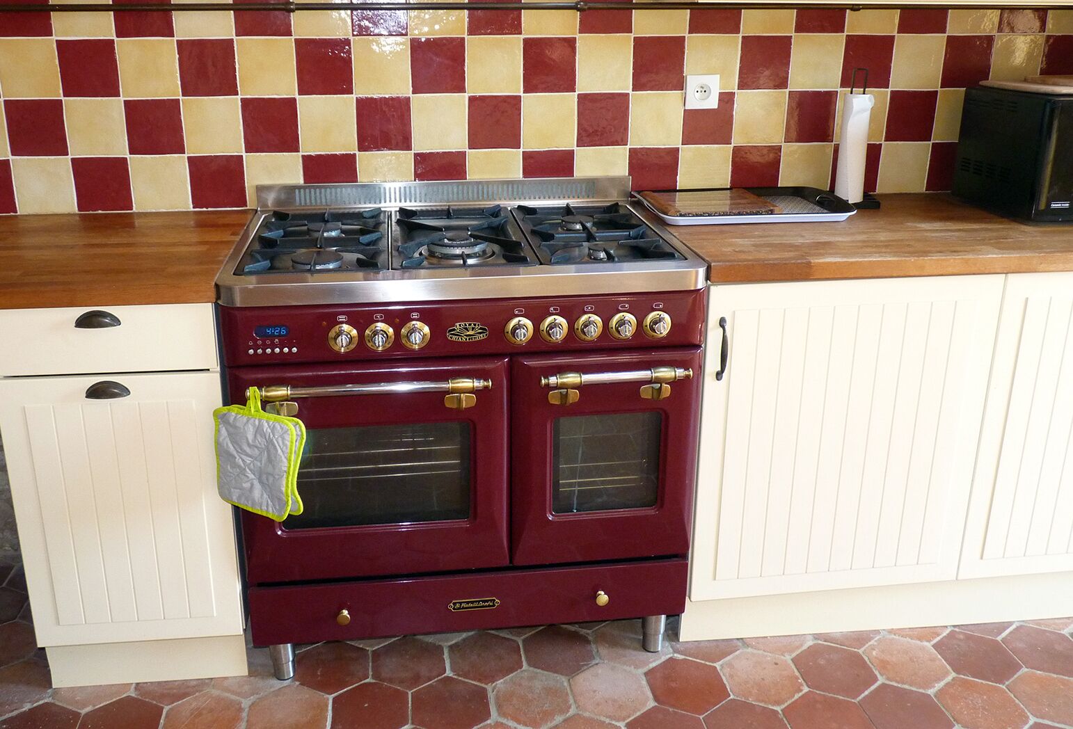 Estufa roja antigua con cuatro hornillas y dos hornos, un armario blanco con cajón y un revoque de azulejos.