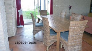 A dining area with a wooden table and wicker chairs, a red curtain, and a view of the outdoors. - Le Petit Cloucq (Damvix)