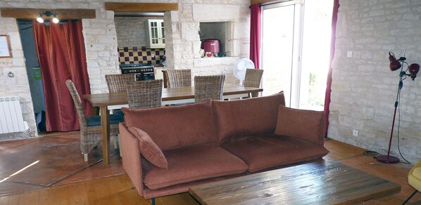 A cozy living room with a brown sofa, wicker chairs, a wooden dining table, and a stone wall.