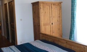 A bedroom with a wooden wardrobe, a bed with patterned bedding, and a window with curtains.