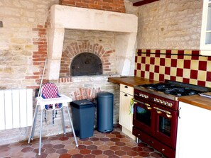 A kitchen with a brick oven, a gas stove, and a tiled backsplash.