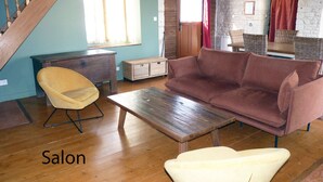 A salon with a wooden floor, a brown sofa, a yellow chair, a wooden table, and a staircase. - Le Petit Cloucq (Damvix)