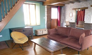 Un salon avec un plancher en bois, un canapé marron, une chaise jaune, une table en bois et un escalier.