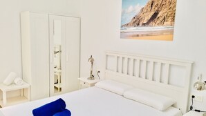 Una habitación de hotel con una cama, un armario, una mesita de noche y un cuadro de una playa.