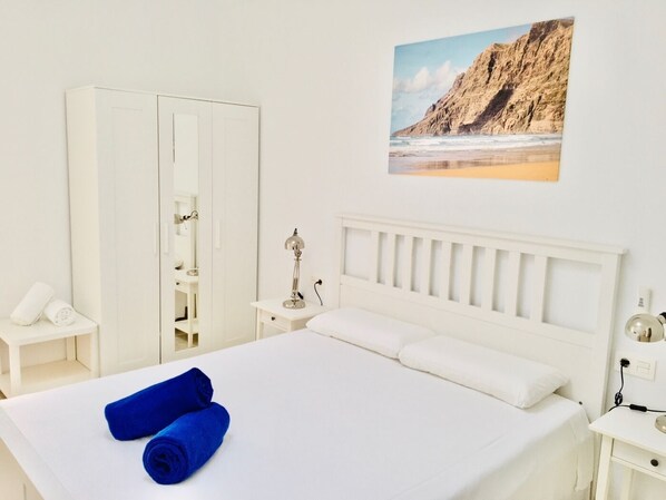 A hotel room with a bed, a wardrobe, a nightstand, and a painting of a beach.
