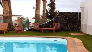 A swimming pool with a stone wall and palm trees. - One bedroom apartment (TAHICHE)