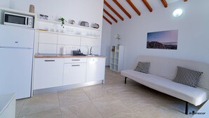 A modern kitchen with white cabinets, a microwave, and a coffee machine. There is a white sofa with patterned cushions in the living area. - One bedroom apartment with terrace. (TAHICHE)