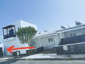 Een modern wit gebouw met een balkon, een cactus voor ernaast en een stenen muur.