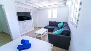 A modern, well-lit room with a bed, a grey sofa, and a TV mounted on the wall. - One bedroom double apartment whit terrace (TAHICHE)