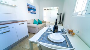 A modern kitchen with white cabinets, a dining table set with plates, glasses, and a bottle. A beige sofa with turquoise cushions is in the background. - One bedroom apartment with pool views (TAHICHE)