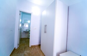 Un couloir étroit donnant sur une salle de bain équipée d’un lavabo, d’un miroir et d’une armoire blanche.