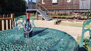 Une table avec une bouteille de vin et des verres, disposée à l’extérieur, avec un wagon de train d’époque en arrière-plan.