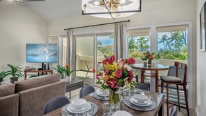 Comedor con mesa lista para cuatro personas, televisor en la pared y balcón con vista a palmeras.