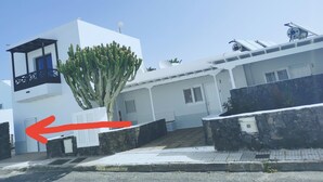 Un edificio moderno blanco con un balcón, un cactus al frente y un muro de piedra.