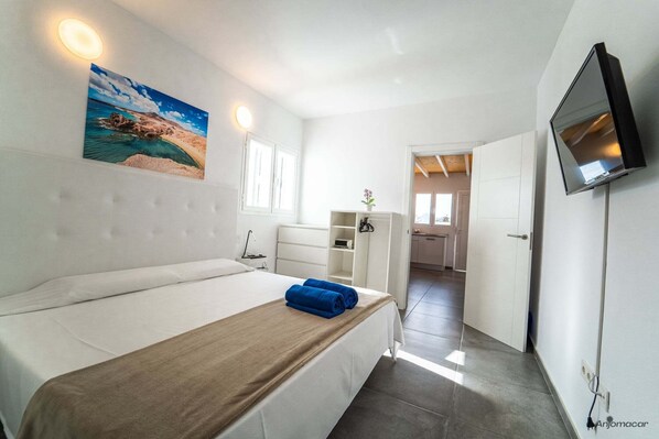A modern hotel room with a bed, a flat-screen TV, a painting, and a view of the sea.