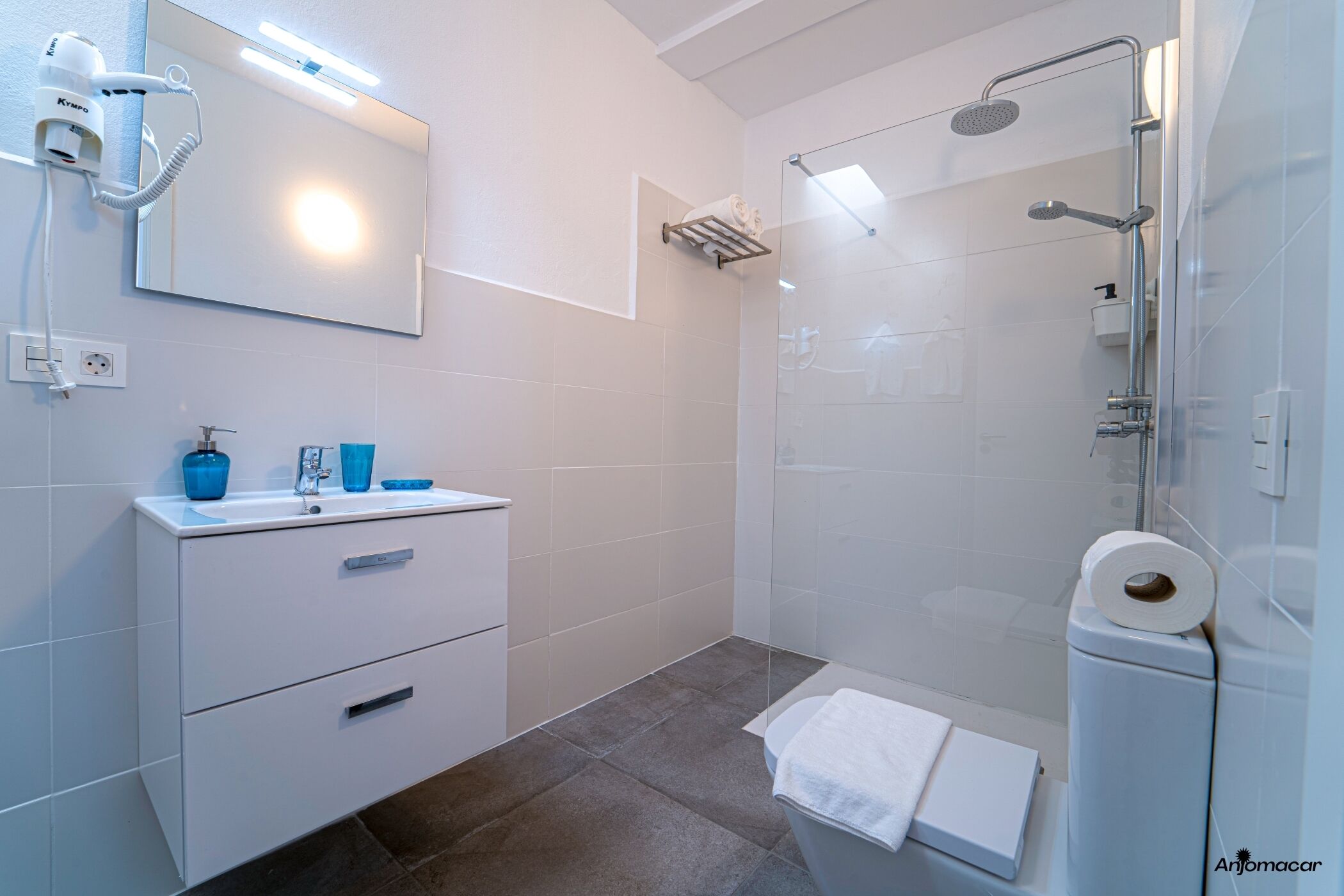 Une salle de bain moderne avec un meuble-lavabo blanc, une cabine de douche en verre et un sèche-cheveux fixé au mur.