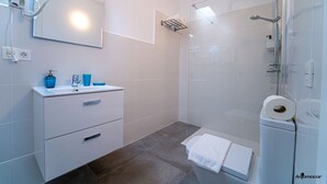 Une salle de bain moderne avec un meuble-lavabo blanc, une cabine de douche en verre et un sèche-cheveux fixé au mur.