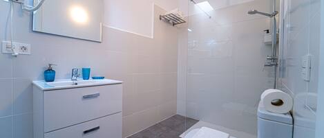 Une salle de bain moderne avec un meuble-lavabo blanc, une cabine de douche en verre et un sèche-cheveux fixé au mur.